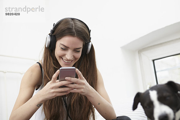 Junge Frau mit Hund auf dem Bett sitzend  Musik hörend