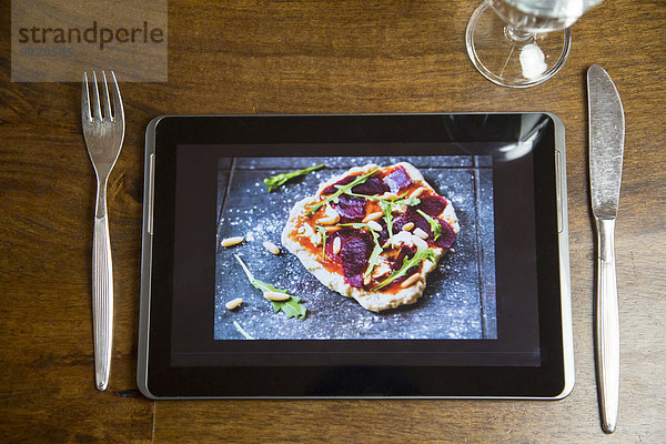 Digitales Tablett mit Lebensmittelfotografie  Glas und Besteck auf Holz