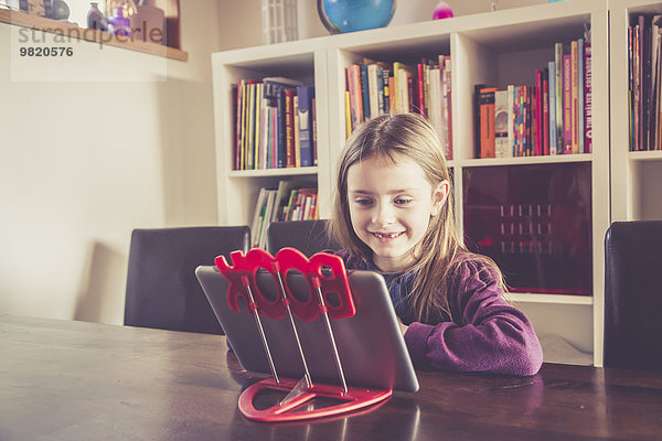 Kleines Mädchen mit digitalem Tablett vor dem Bücherregal
