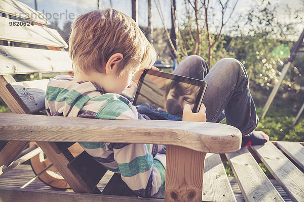 Junge spielt mit digitalem Tablett auf Holzliegestuhl