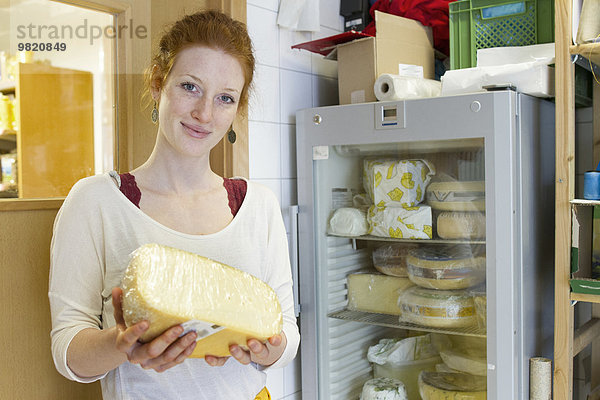 Porträt einer lächelnden jungen Frau im Vollwertladen mit einem Stück Käse