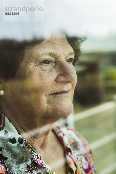 Porträt einer älteren Frau mit Blick durchs Fenster