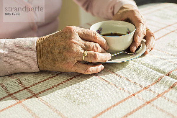 Hände einer älteren Frau  die eine Tasse Kaffee hält.