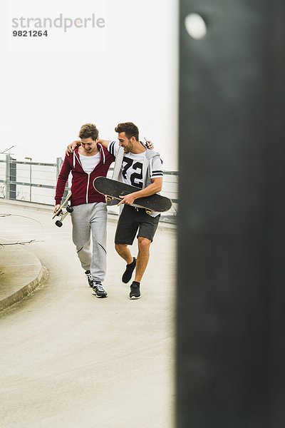 Zwei glückliche Freunde  die mit Skateboards spazieren gehen.
