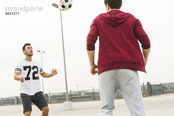 Zwei junge Männer beim Fußballspielen auf dem Parkdeck