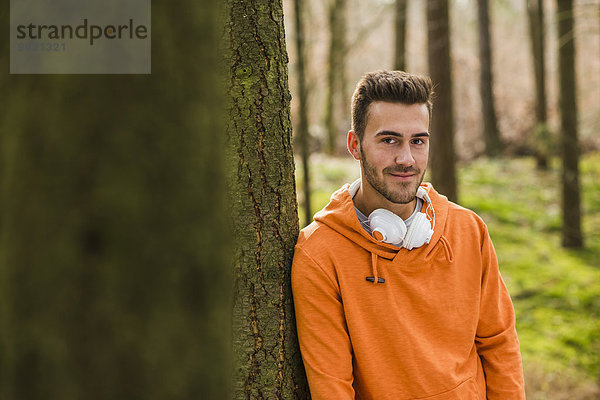 Lächelnder junger Mann mit Kopfhörer im Wald