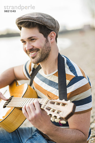 Mann am Flussufer sitzend  Gitarre spielend