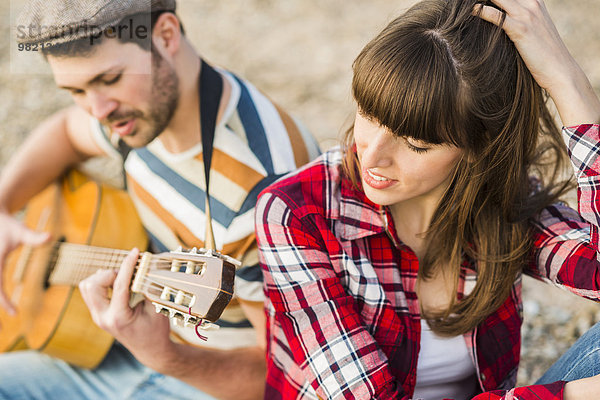 Paar am Flussufer sitzend  Gitarre spielend