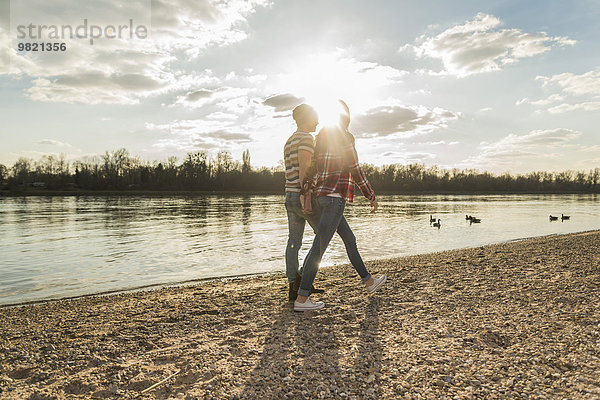 Glückliches junges Paar am Flussufer geht Hand in Hand