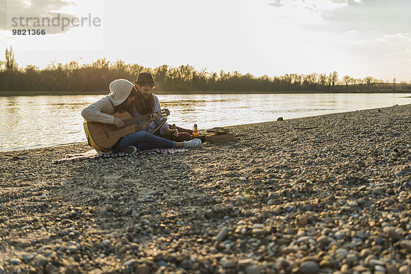 Paar am Flussufer beim Gitarrespielen