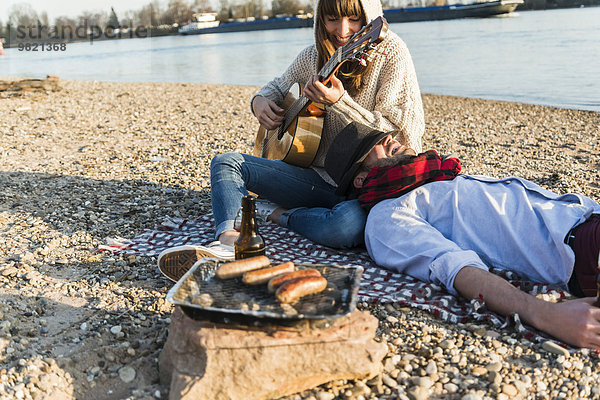 Paar am Flussufer sitzend  Gitarre spielend
