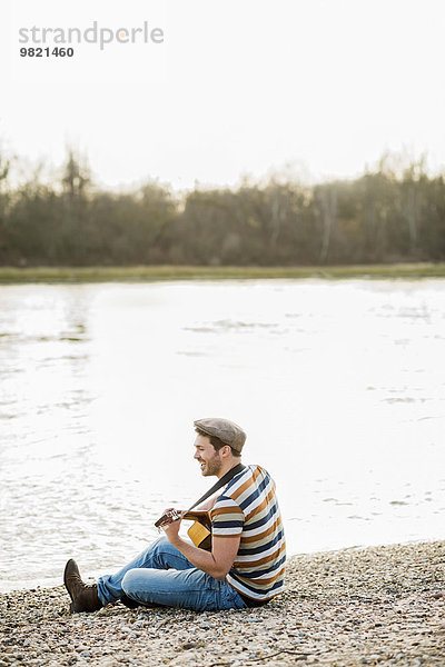 Mann am Flussufer sitzend  Gitarre spielend