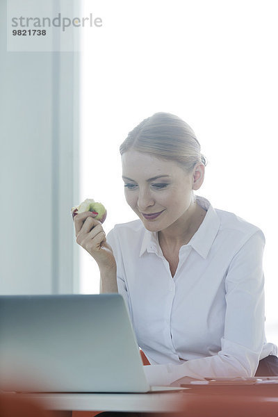 Geschäftsfrau sitzt am Schreibtisch und isst Apfel