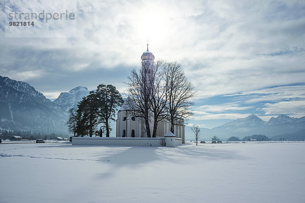 Deutschland  Bayern  Blick auf die St. Coloman Kirche vor dem Tannheimer Gebirge im Winter