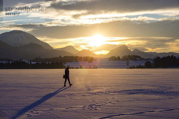 Deutschland  Hopfensee  Frau beim Spaziergang in der Winterlandschaft bei Sonnenuntergang