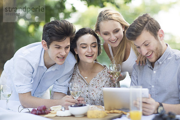 Freunde beim Essen im Freien und mit digitalen Tabletts