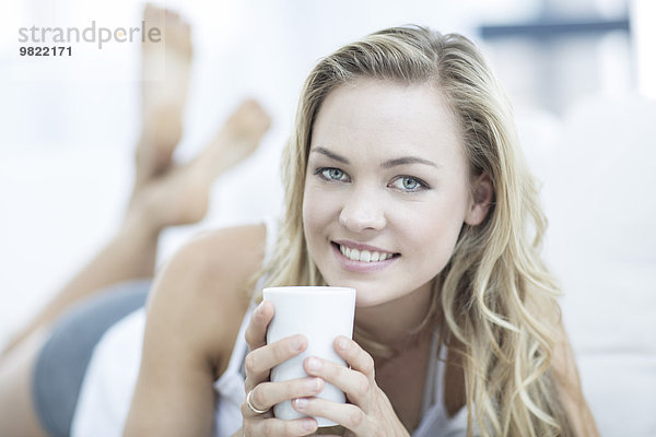 Porträt einer blonden Frau auf einer Couch mit einer Tasse Kaffee