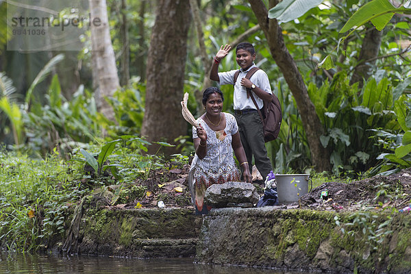 Junge und Frau winkend  Kanalsystem Backwaters  bei Alappuzha  Kerala  Indien  Asien