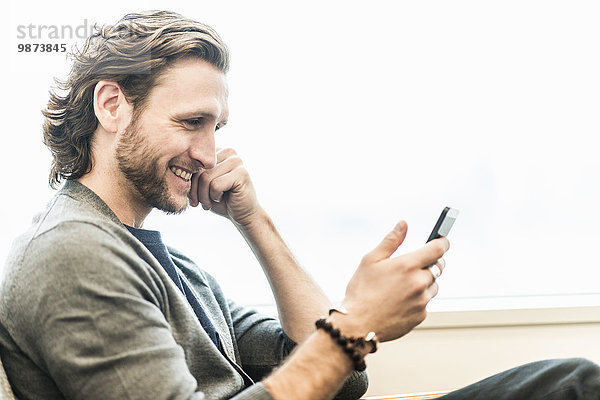Ein bärtiger Mann sitzt lächelnd und schaut auf sein Telefon.