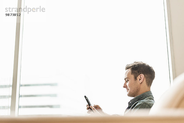 Ein Mann sitzt mit einem Smartphone in der Hand und hört seine Nachrichten ab.