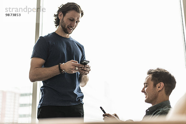 Zwei Männer in einem Büro  die ihre Smartphones überprüfen.