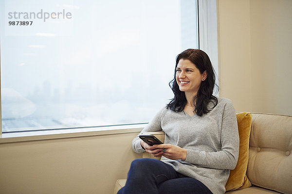 Eine Geschäftsfrau sitzt an einem Fenster und hält ein Smartphone in der Hand.