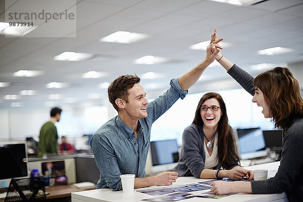 Drei Personen in einem Büro  die sich Fotos anschauen und eine High-Five-Geste machen.
