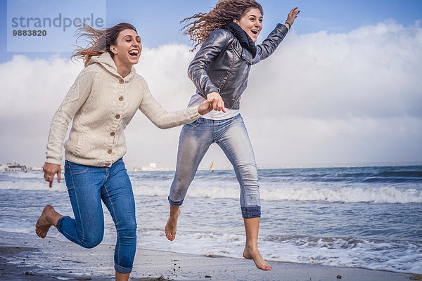 Zwei junge Frauen  die am Strand rennen und springen.