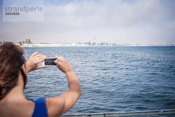 Junge Frau fotografiert Meerblick auf dem Smartphone