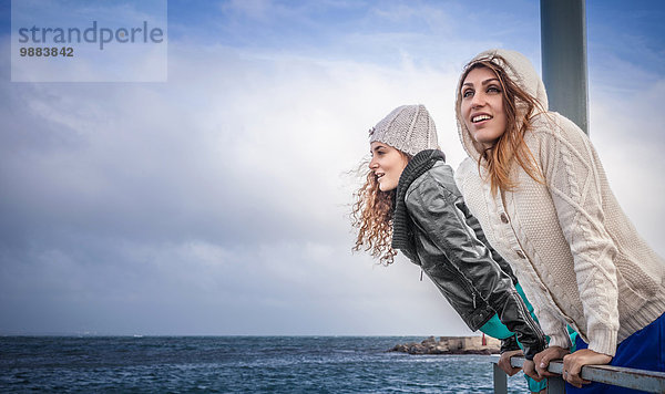 Zwei junge Frauen  die vom Pier aus auf das Meer schauen.