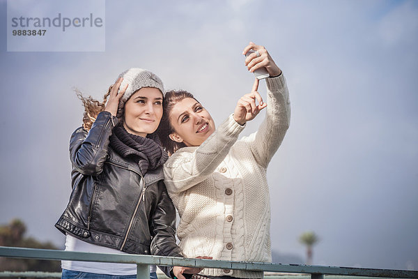 Zwei junge Freundinnen mit Touchscreen für Smartphone Selfie an der Küste