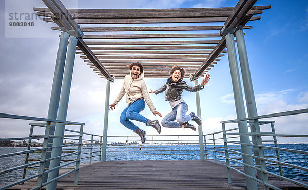 Zwei junge Freundinnen springen unisono auf der Seebrücke.