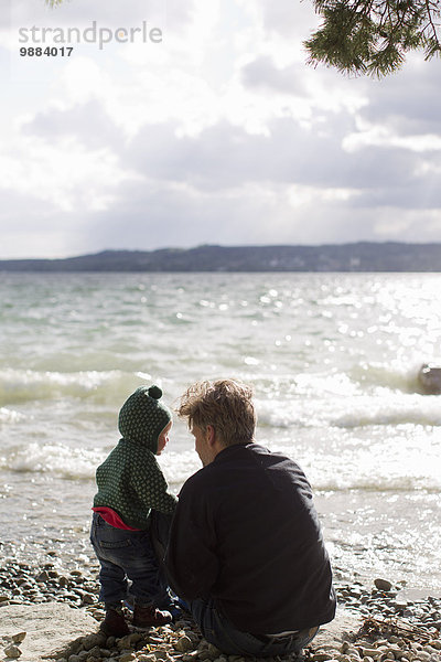 Vater und Tochter hocken am Seeufer  Starnberger See  Bayern  Deutschland
