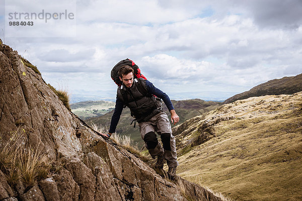 Junge männliche Wanderer  die aus dem Felsen steigen  The Lake District  Cumbria  UK