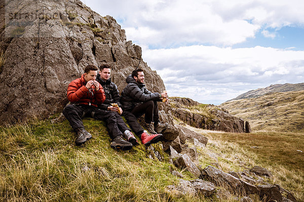 Drei junge männliche Wanderfreunde essen Sandwiches  The Lake District  Cumbria  UK