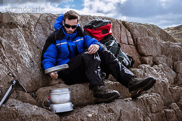 Junger Kletterer auf Felsen  der den Campingkocher vorbereitet  The Lake District  Cumbria  UK