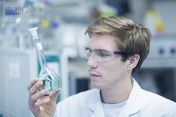 Männlicher Wissenschaftler hält sich hoch und schaut sich die Flasche im Labor an.