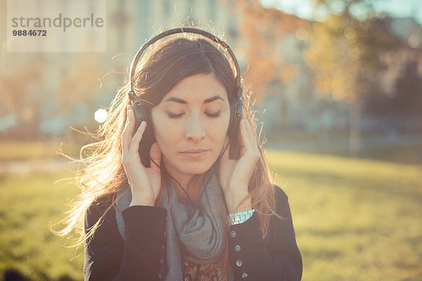Mittlere erwachsene Frau mit geschlossenen Augen  die Kopfhörer im Park hört.