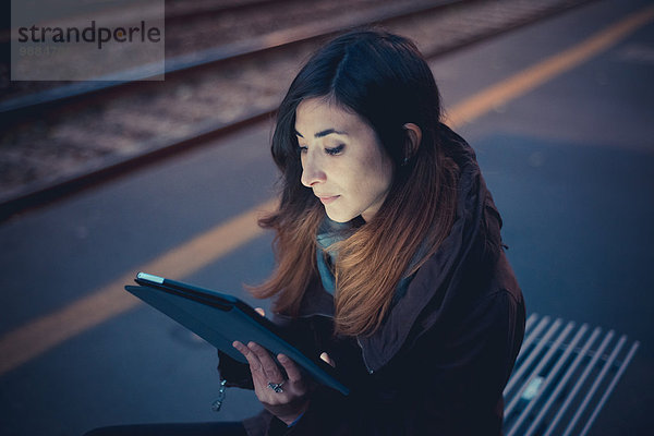 Mittlere erwachsene Frau mit digitalem Tablett auf dem Bahnsteig in der Abenddämmerung