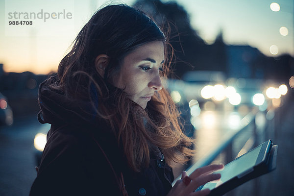 Mittlere erwachsene Frau mit digitalem Tablett-Touchscreen auf der Straße in der Abenddämmerung