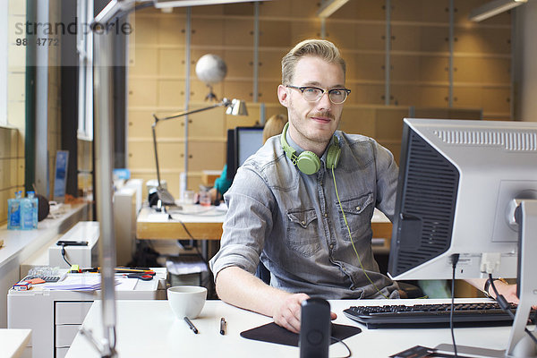 Porträt eines jungen Mannes mit Computer am Schreibtisch