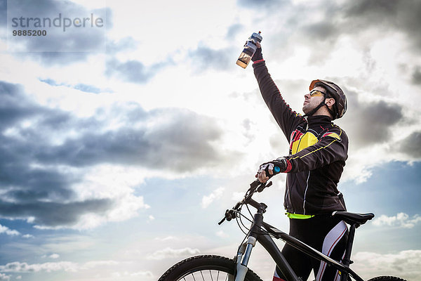 Mittlerer Erwachsener männlicher Mountainbiker feiert mit Wasserflasche