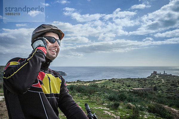 Mittlerer Erwachsener  männlicher Mountainbiker beim Chatten auf dem Smartphone vom Küstenweg aus  Cagliari  Sardinien  Italien