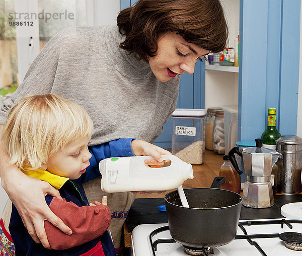 Mutter und Sohn gießen Milch in die Breipfanne in der Küche.