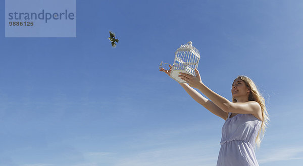 Junge Frau befreit Vogel aus dem Käfig in Richtung blauer Himmel