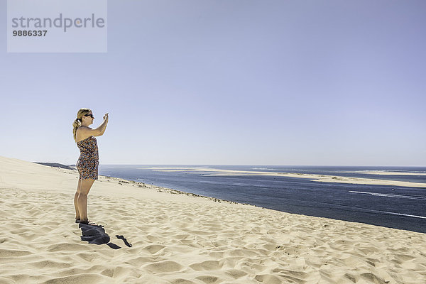 Junge Frau fotografiert Meer mit Smartphone  Dune de Pilat  Frankreich