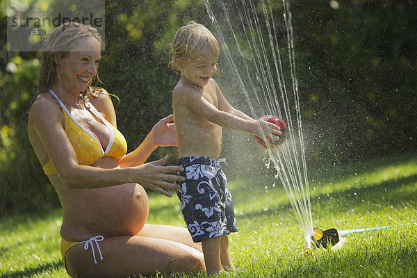 sitzend Sohn Bikini nass Rasen Rasensprenger Schwangerschaft Spiel jung Verbindung Mutter - Mensch