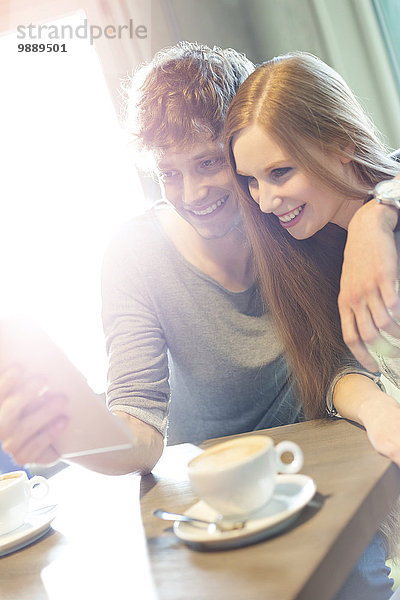 Lächelndes Paar nimmt Selfie mit digitalem Tablett im sonnigen Cafe