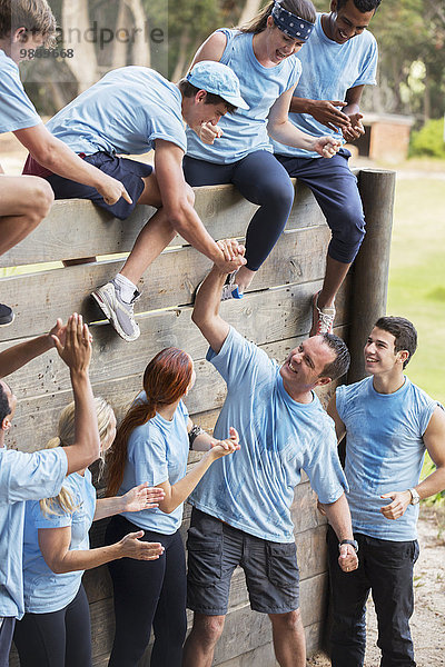 Teamkollegen helfen sich gegenseitig über die Wand auf dem Hindernisparcours des Bootcamps.