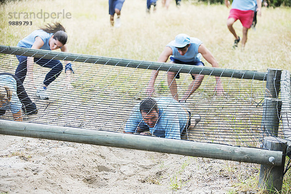 Menschen krabbeln unter dem Netz auf dem Bootcamp-Hindernisparcours